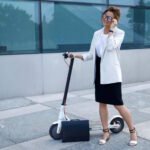 Businesswoman in a white blazer standing with an electric scooter and a briefcase, representing eco-friendly urban commuting.