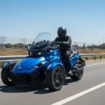 Person riding a blue three-wheeled motorcycle on a highway under a clear sky, wearing a black helmet and leather jacket for safety.