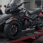 A mechanic working on a Can-Am Spyder three-wheeled motorcycle in a professional workshop. The vehicle is elevated on a red maintenance platform, surrounded by various tools and equipment mounted on the wall and workbenches.
