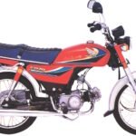 Side view of a Honda CD70 motorcycle with a bright red fuel tank, blue seat, chrome exhaust and forks, and wire-spoke wheels. The small commuter bike features the Honda logo and CD70 badging on its bodywork.