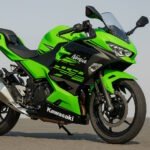 A high-resolution side view of a Kawasaki Ninja 400 motorcycle in Kawasaki Green with black graphics, parked on a textured pavement under a clear sky.