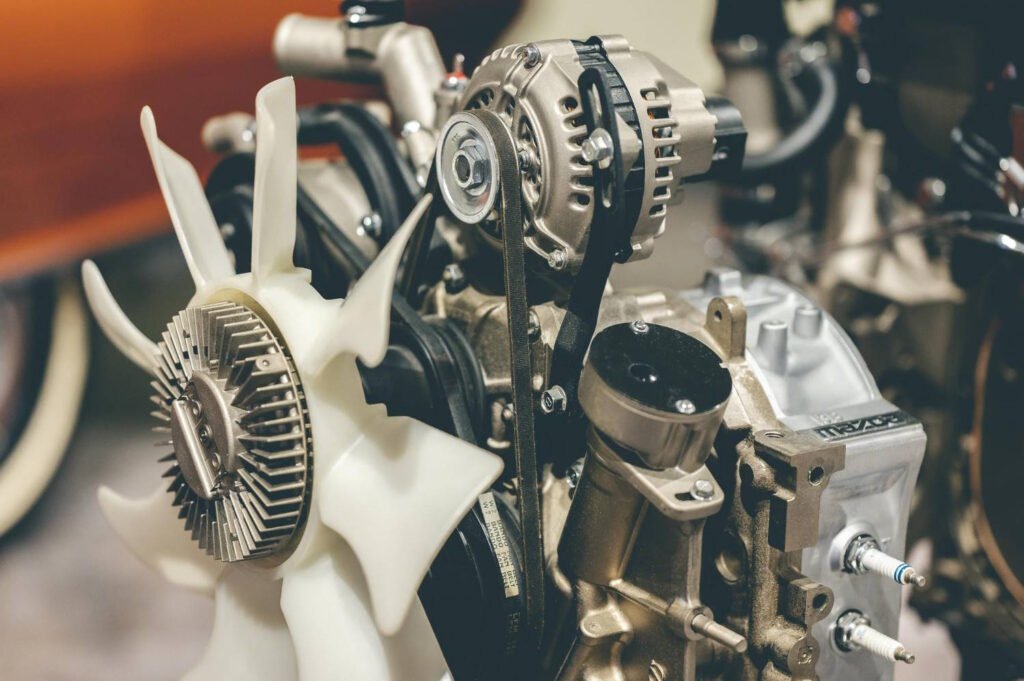 Close-up of a car engine showing the fan, alternator, and belt system—highlighting how worn engine or transmission mounts can lead to noticeable vibrations in the steering wheel, especially during acceleration or steady-speed driving.