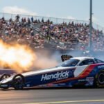 Brittany Force's Top Fuel dragster with HendrickCars.com livery launching off the line with flames from the exhaust and a cheering crowd in the background.