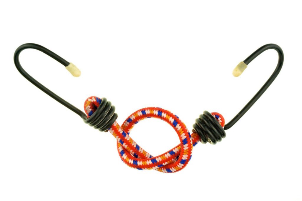 A red, blue, and white braided bungee cord featuring black metal hooks with rubber tips, coiled for compact storage, ideal for securing cargo or motorcycle gear.