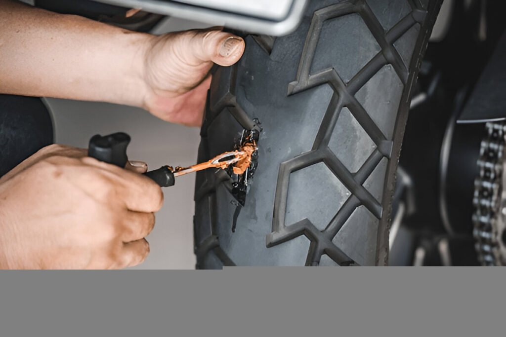 Close-up of hands repairing a motorcycle tire using a plug kit, with a rubber plug being inserted into the puncture in the tread.