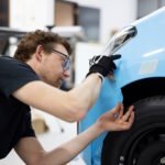 Professional applying vinyl wrap to a car fender, illustrating the process and detail involved in how much does a vehicle wrap cost