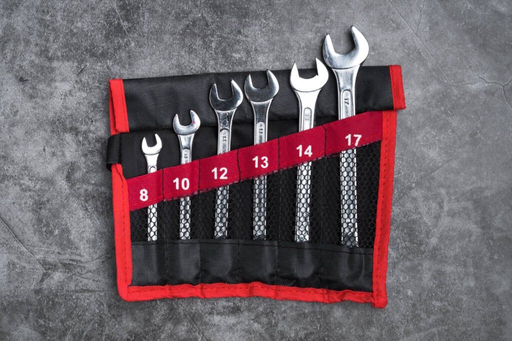 A neatly arranged set of open-end wrenches in sizes 8mm to 17mm, stored in a black and red roll-up pouch, displayed on a textured concrete surface.