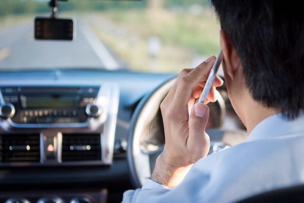 Person holding a cell phone to their ear while sitting in the driver's seat of a car, demonstrating distracted driving behavior