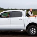 White Ford Maverick pickup truck with driver and passenger in farm field