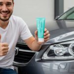 Man smiling and giving thumbs up while holding a tube of toothpaste next to a car with headlights, demonstrating an easy DIY method for cleaning foggy headlights.