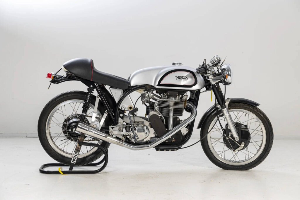 Classic Norton racing motorcycle with silver fuel tank, black frame and seat, displayed on a stand against a white background.