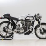 Classic Norton racing motorcycle with silver fuel tank, black frame and seat, displayed on a stand against a white background.