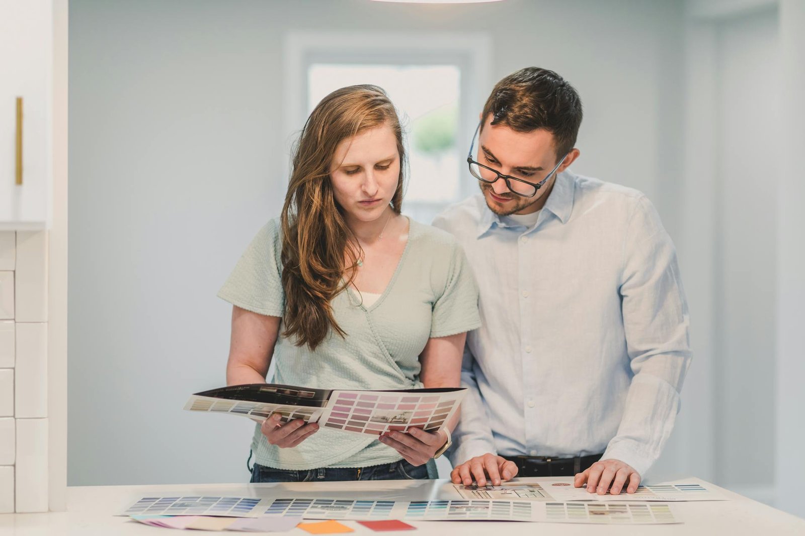 Young couple planning home renovation looking at color palette samples and design materials on kitchen counter in bright modern home
