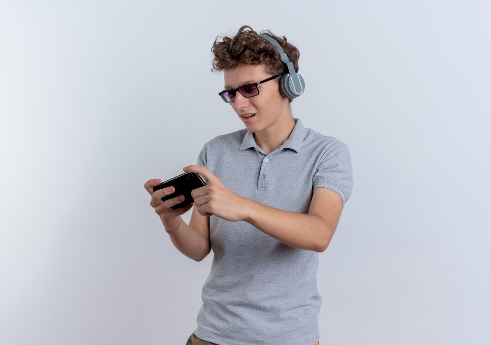 Young man with curly hair wearing sunglasses and headphones, playing games on one of the best gaming phones under £300 against a white background